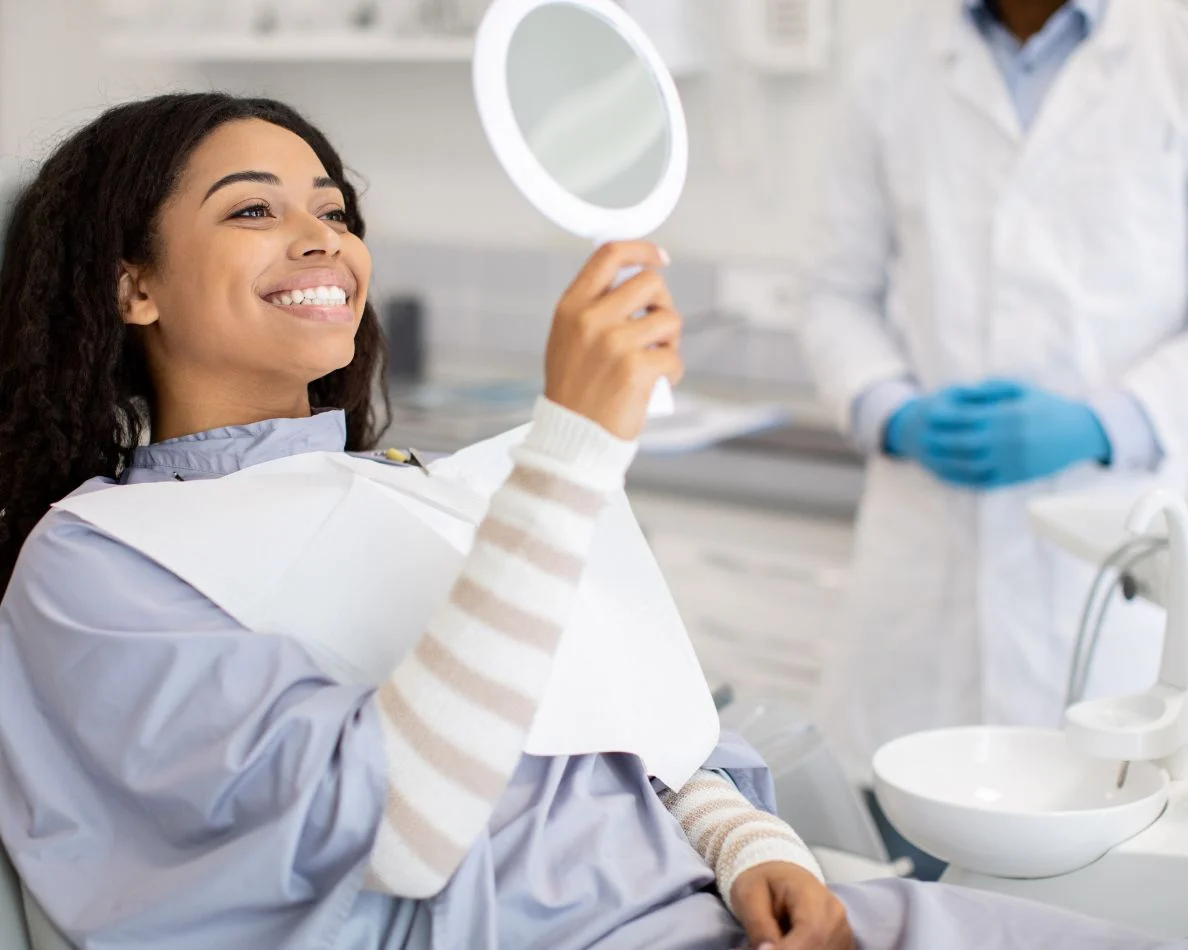 Paciente sonriendo con un espejo de mano junto a su dentista